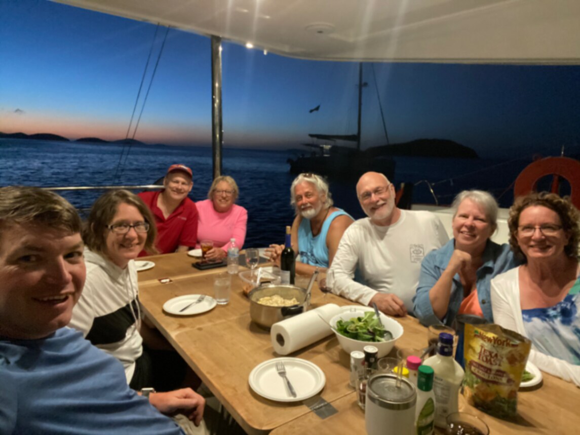 Crew gathered around the cockpit table for dinner aboard the catamaran at dusk