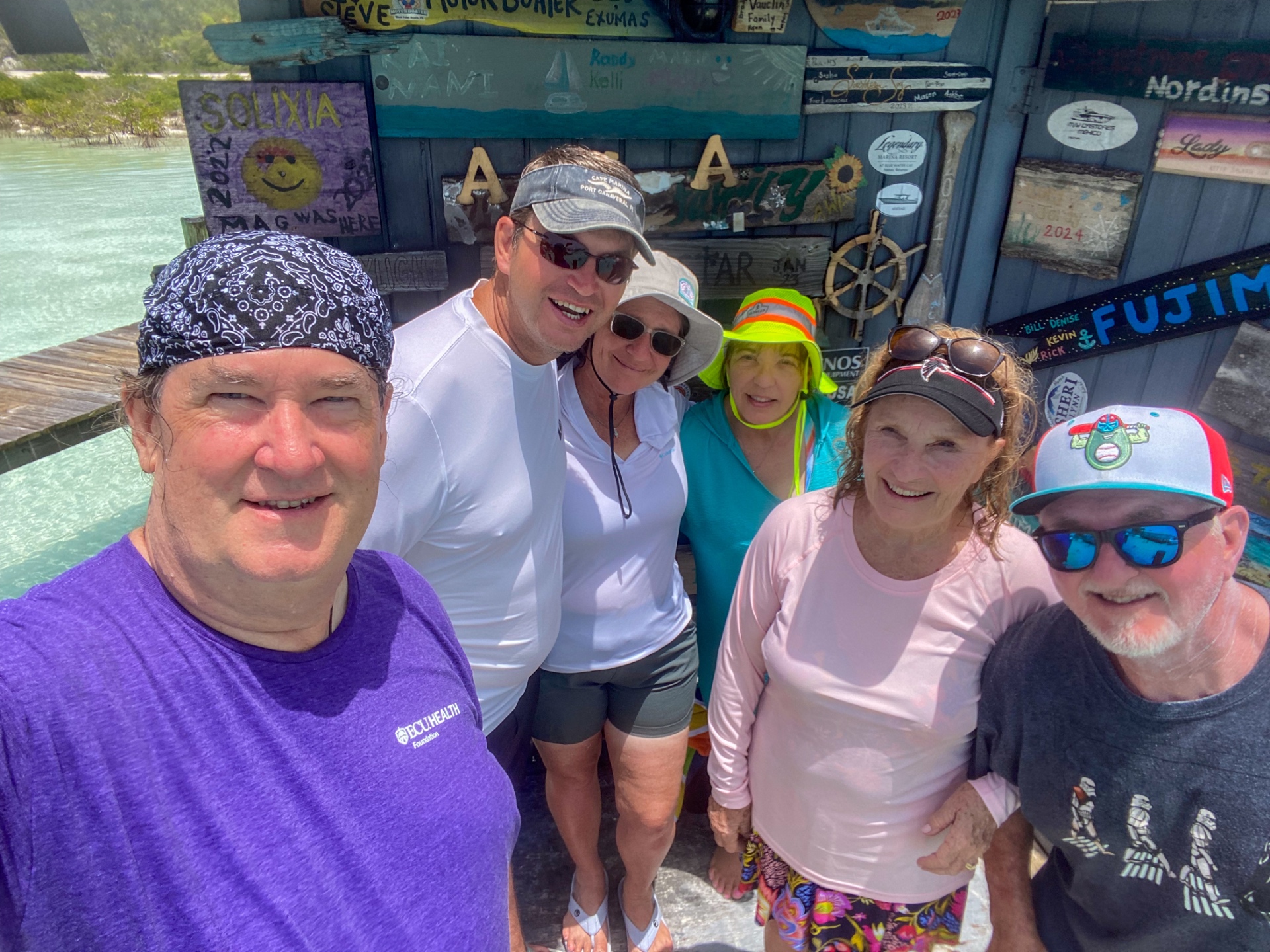 Group of friends at a dockside hut covered in boat name plaques in the Exumas, Bahamas